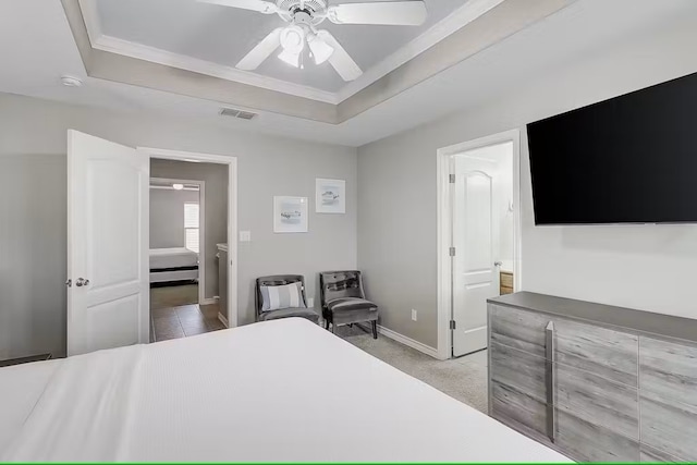 bedroom with ceiling fan, ensuite bath, light carpet, and a raised ceiling