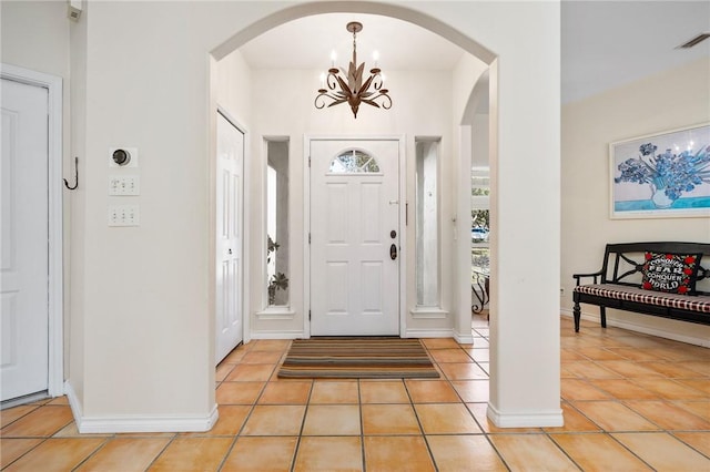 entrance foyer with light tile patterned floors, baseboards, visible vents, arched walkways, and a notable chandelier