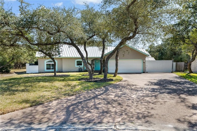 ranch-style house featuring a standing seam roof, an attached garage, fence, and stucco siding