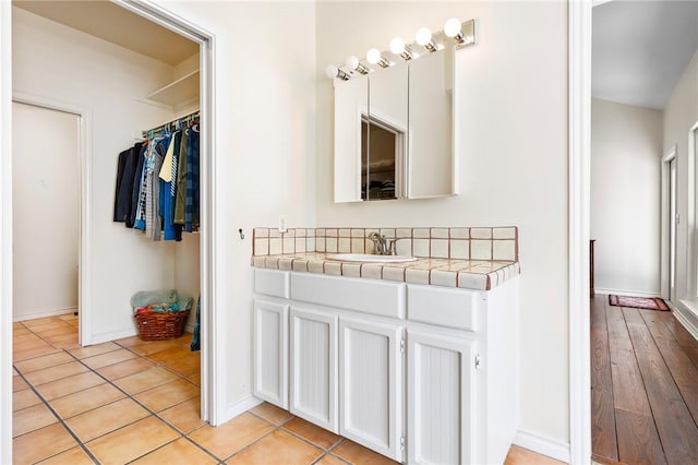 bathroom with tile patterned floors, baseboards, a walk in closet, and vanity