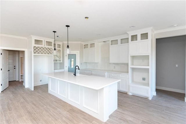 kitchen with white cabinetry, an island with sink, and ornamental molding