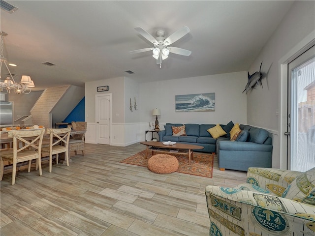 living room featuring ceiling fan with notable chandelier and light hardwood / wood-style flooring