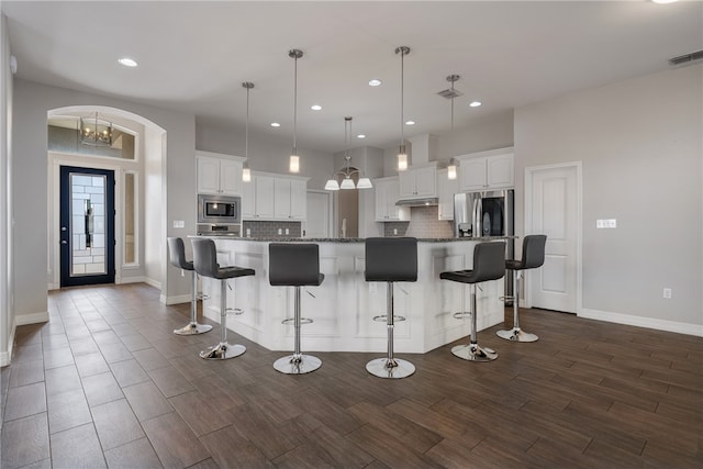 kitchen featuring hanging light fixtures, stainless steel appliances, a spacious island, a breakfast bar, and white cabinets