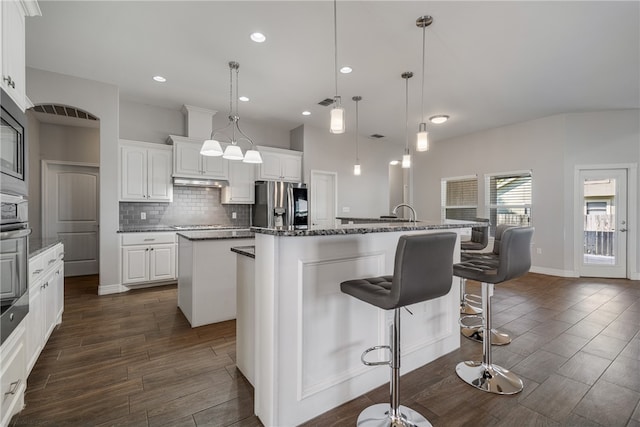 kitchen featuring white cabinetry, stainless steel fridge, an island with sink, and pendant lighting