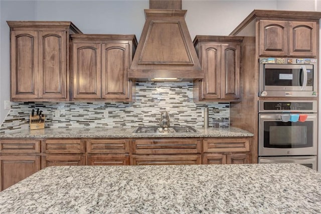 kitchen with tasteful backsplash, light stone countertops, custom range hood, and appliances with stainless steel finishes