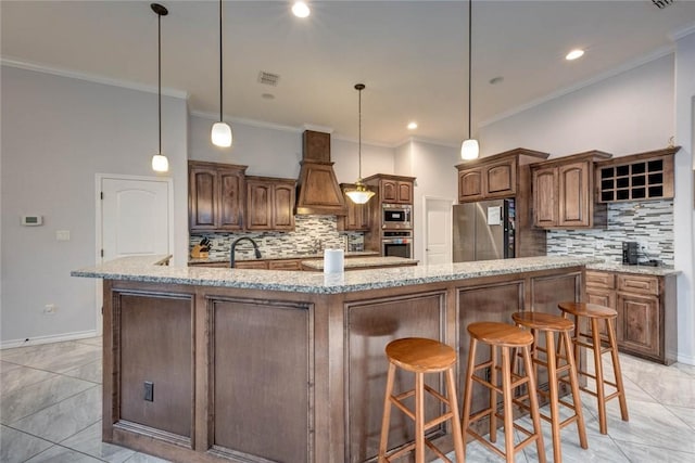 kitchen featuring a large island with sink, tasteful backsplash, decorative light fixtures, light stone counters, and stainless steel appliances