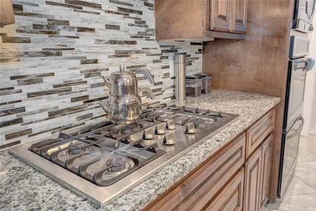 kitchen featuring light tile patterned floors, light stone countertops, backsplash, and stainless steel gas cooktop