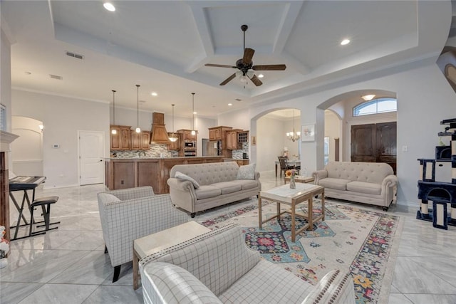 living room with a tray ceiling, crown molding, and ceiling fan with notable chandelier