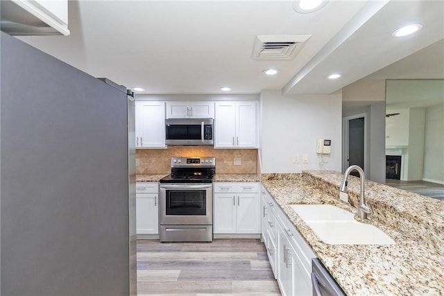 200 W Cotter Ave Unit B-3, Port Aransas, TX 78373 - kitchen featuring appliances with stainless steel finishes, a sink, light wood-style floors, white cabinets, and light stone counters
