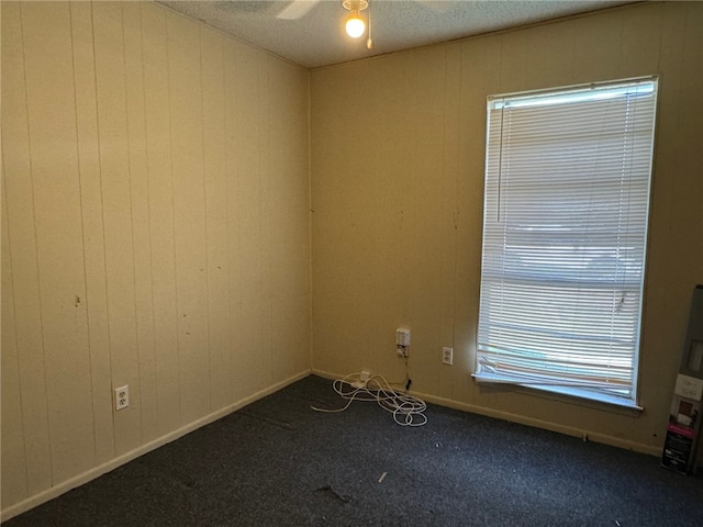 empty room featuring carpet flooring, a textured ceiling, wood walls, and ceiling fan