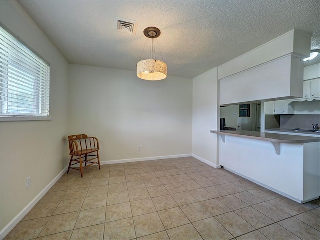 1638 Spicewood Dr, Corpus Christi, TX 78412 - kitchen featuring a breakfast bar, white cabinetry, a peninsula, hanging light fixtures, and a textured ceiling