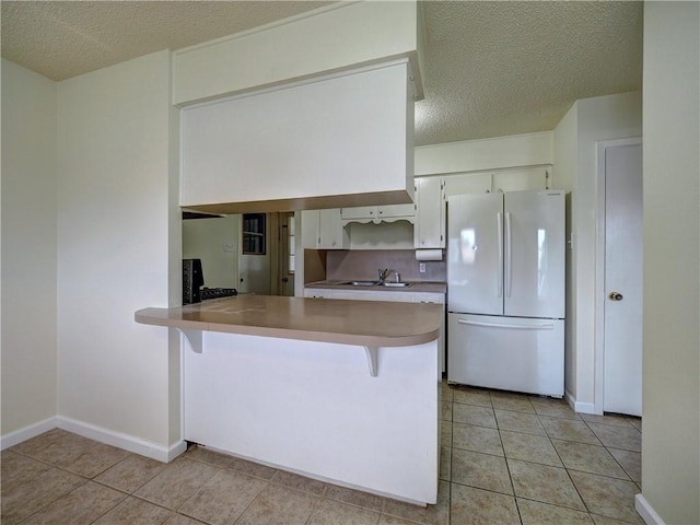 1638 Spicewood Dr, Corpus Christi, TX 78412 - kitchen featuring freestanding refrigerator, a textured ceiling, a peninsula, white cabinetry, and light tile patterned flooring