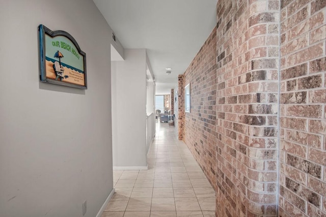 corridor featuring light tile patterned floors and brick wall