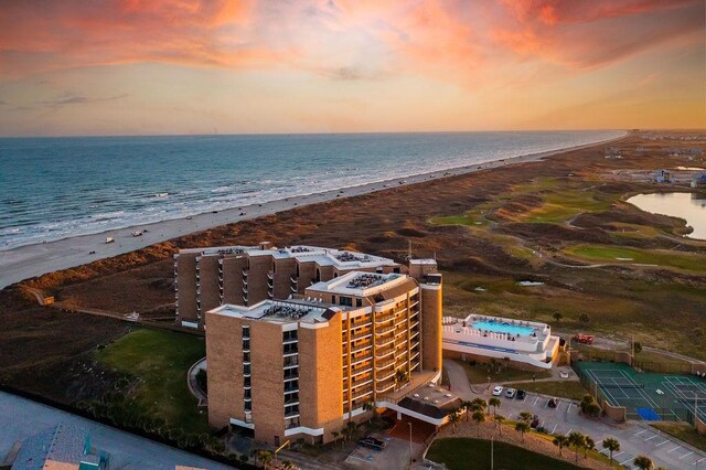 aerial view at dusk featuring a view of the beach and a water view