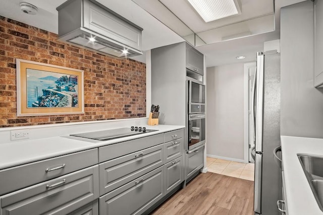 kitchen featuring brick wall, black electric stovetop, stainless steel fridge, and gray cabinetry