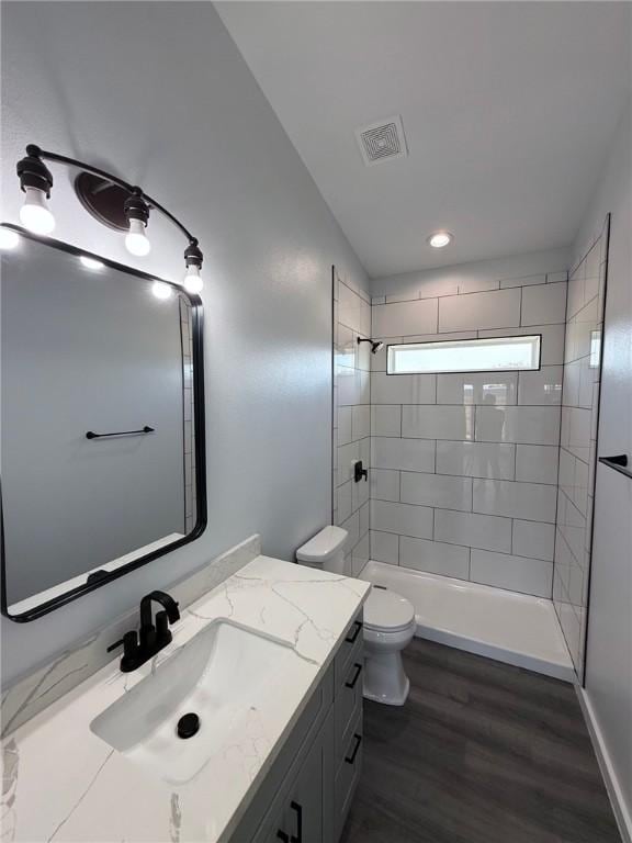 bathroom with vanity, hardwood / wood-style flooring, tiled shower, and toilet