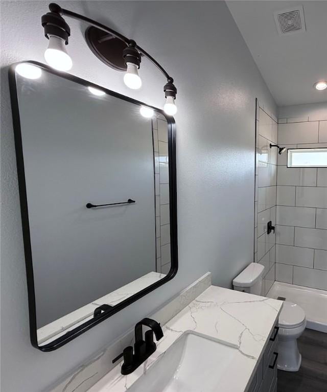 bathroom featuring a tile shower, toilet, and vanity