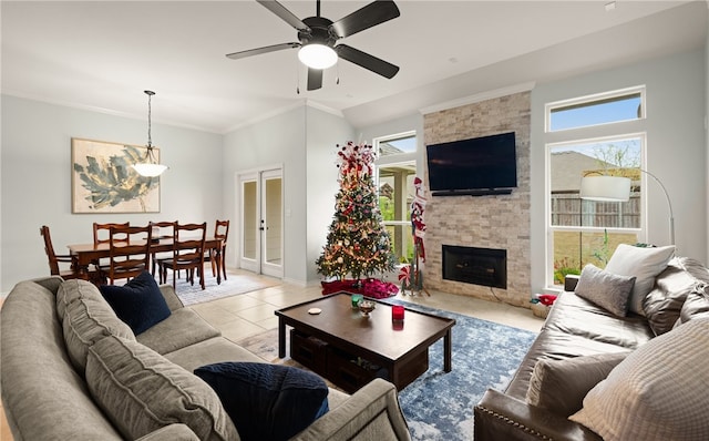 living room with a stone fireplace, ceiling fan, crown molding, and light tile patterned flooring