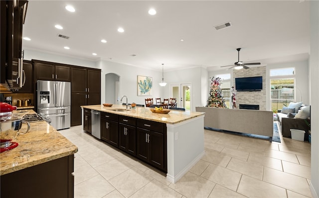 kitchen with sink, hanging light fixtures, stainless steel appliances, light stone counters, and an island with sink