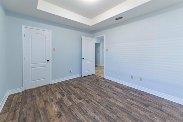 spare room featuring dark wood-type flooring, a tray ceiling, visible vents, and baseboards