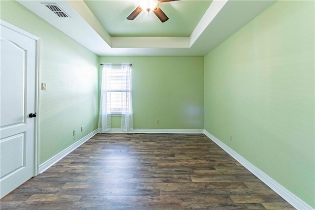 empty room featuring visible vents, baseboards, a ceiling fan, dark wood-style floors, and a raised ceiling