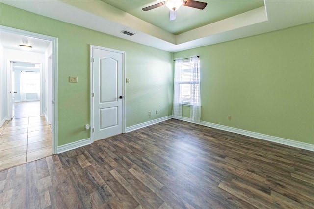 spare room featuring a tray ceiling, visible vents, dark wood-type flooring, a ceiling fan, and baseboards