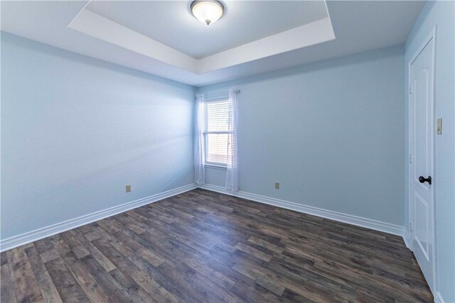 unfurnished room with a tray ceiling, dark wood-style flooring, and baseboards