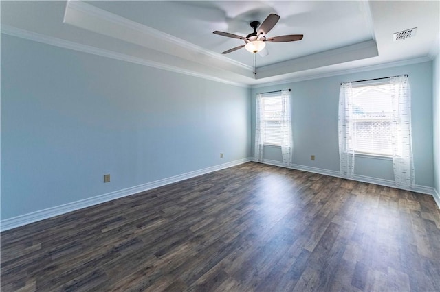 spare room with a tray ceiling, dark wood-style flooring, visible vents, ornamental molding, and baseboards