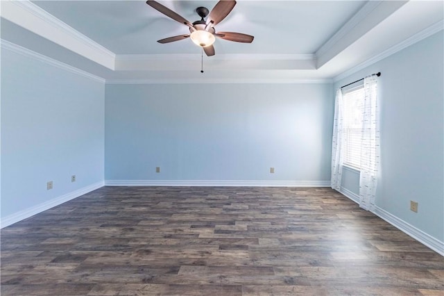 spare room with ornamental molding, a tray ceiling, dark wood finished floors, and baseboards