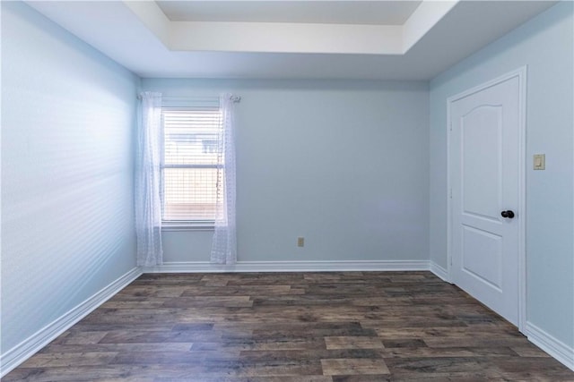 empty room featuring a tray ceiling, dark wood-style flooring, and baseboards