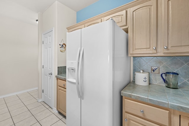 kitchen featuring white refrigerator with ice dispenser, light tile patterned floors, light brown cabinetry, decorative backsplash, and tile countertops