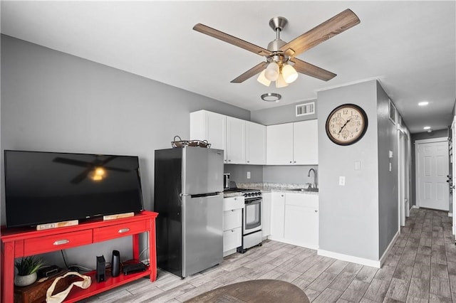 kitchen featuring stainless steel fridge, light wood-type flooring, white range with gas stovetop, sink, and white cabinets