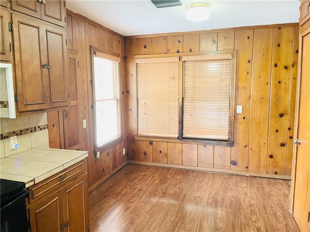 912 E Fulton St, Sinton, TX 78387 - kitchen with tile countertops, light wood-style floors, wooden walls, baseboards, and backsplash