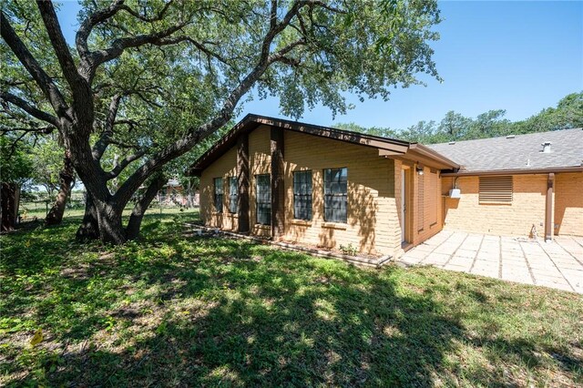 view of property exterior featuring brick siding, a yard, and a patio