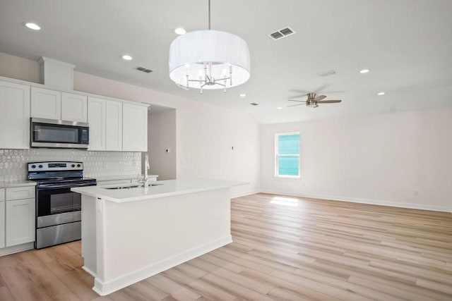 kitchen featuring white cabinetry, tasteful backsplash, decorative light fixtures, appliances with stainless steel finishes, and a kitchen island with sink