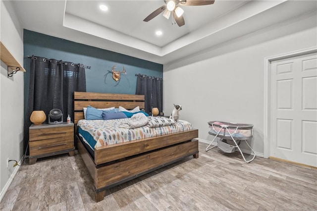 bedroom with hardwood / wood-style floors, a tray ceiling, and ceiling fan