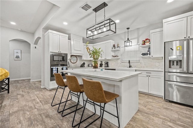 kitchen with light stone countertops, white cabinetry, hanging light fixtures, stainless steel appliances, and a kitchen island