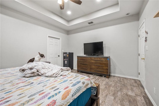 bedroom featuring ceiling fan, light hardwood / wood-style floors, and a tray ceiling