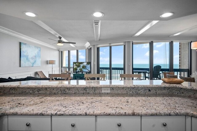 kitchen featuring ceiling fan, a water view, a wainscoted wall, ornamental molding, and white cabinetry