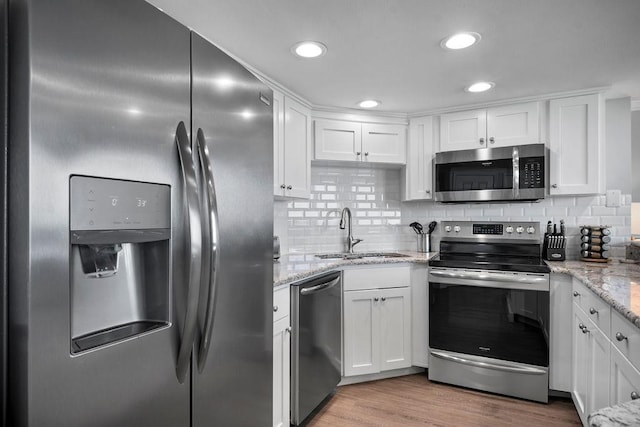 kitchen featuring backsplash, stainless steel appliances, wood finished floors, white cabinetry, and a sink