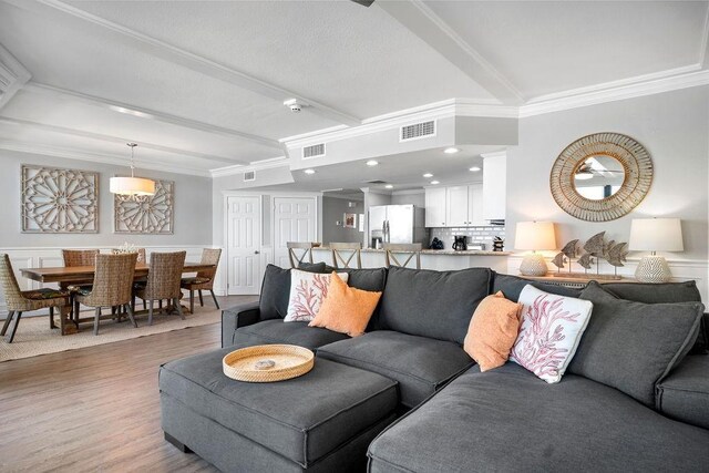 living area with visible vents, beamed ceiling, wood finished floors, and ornamental molding