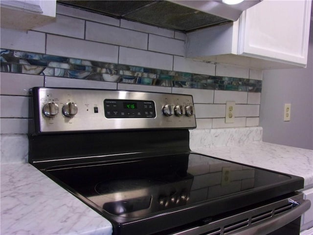 kitchen with backsplash, stainless steel range with electric cooktop, ventilation hood, white cabinets, and light stone countertops