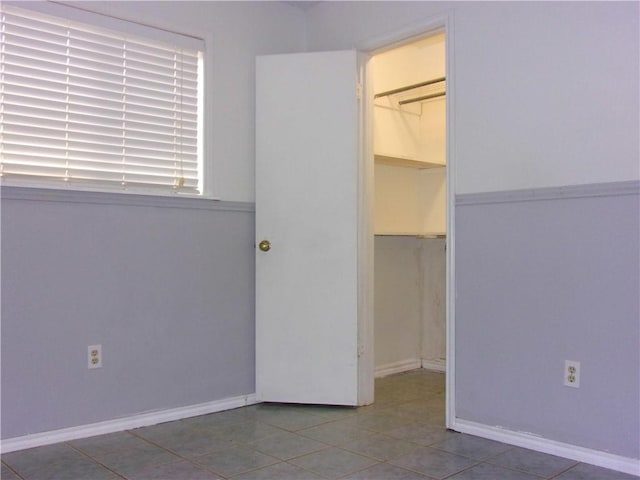 unfurnished bedroom featuring a walk in closet, tile patterned floors, baseboards, and a closet