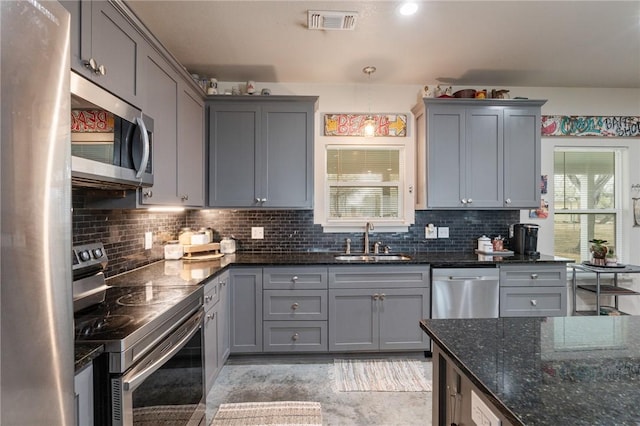 kitchen featuring sink, gray cabinets, dark stone countertops, stainless steel appliances, and tasteful backsplash