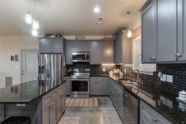 kitchen featuring sink, hanging light fixtures, dark stone counters, a kitchen island, and stainless steel appliances