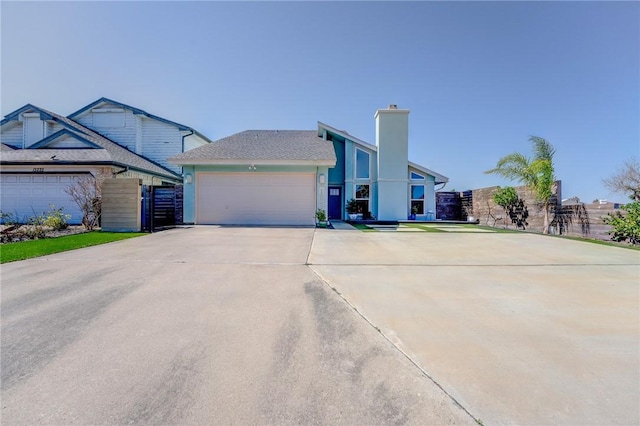 view of front facade with concrete driveway, a chimney, an attached garage, and fence