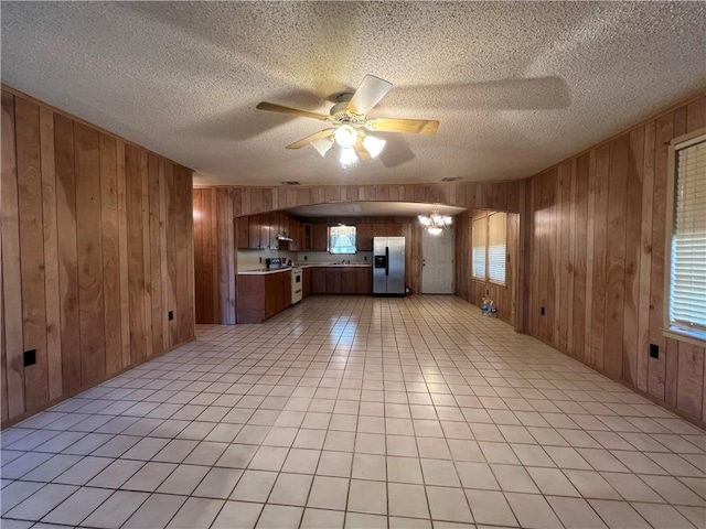 unfurnished living room featuring wooden walls, ceiling fan with notable chandelier, and a textured ceiling