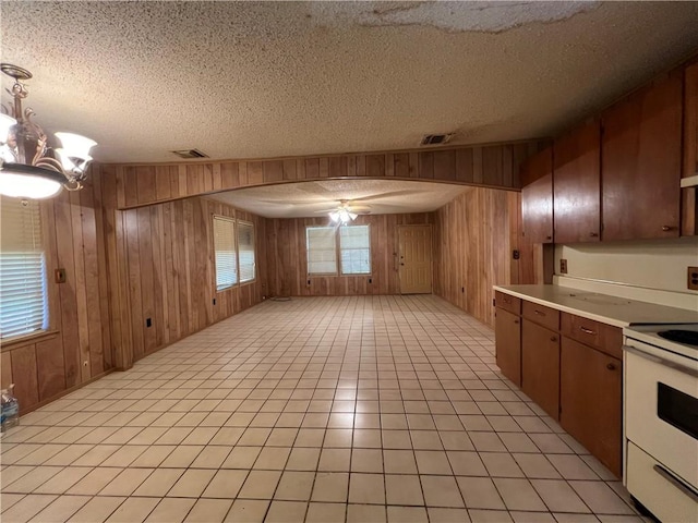 kitchen with hanging light fixtures, white electric range, wood walls, a textured ceiling, and ceiling fan with notable chandelier