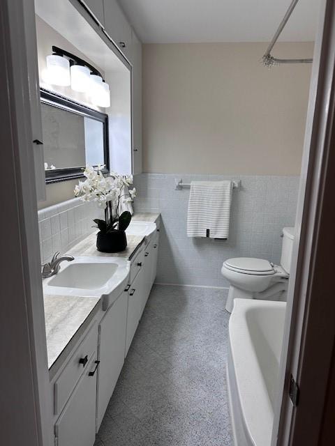 4633 Wilma Dr, Corpus Christi, TX 78412 - bathroom featuring toilet, double vanity, wainscoting, a tub to relax in, and tile walls