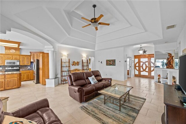 tiled living room with ceiling fan and a raised ceiling